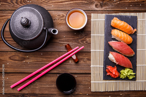 Sushi Set served on gray stone slate with soy sauce, grey teapot and cup of tea