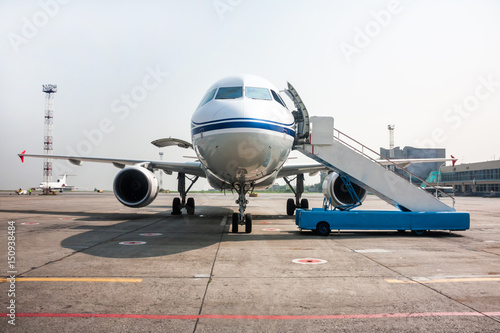 Passenger airplane with open luggage compartment and boarding ramp near at the airport apron