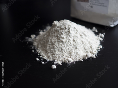 Wholemeal flour in a pile on black wooden table with a flour bag in the background
