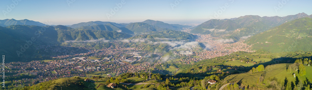 Drone aerial view to the Seriana valley in a clear and blue day. Fog is covering the villages. Panorama from Farno Mountain, Bergamo, Italy.