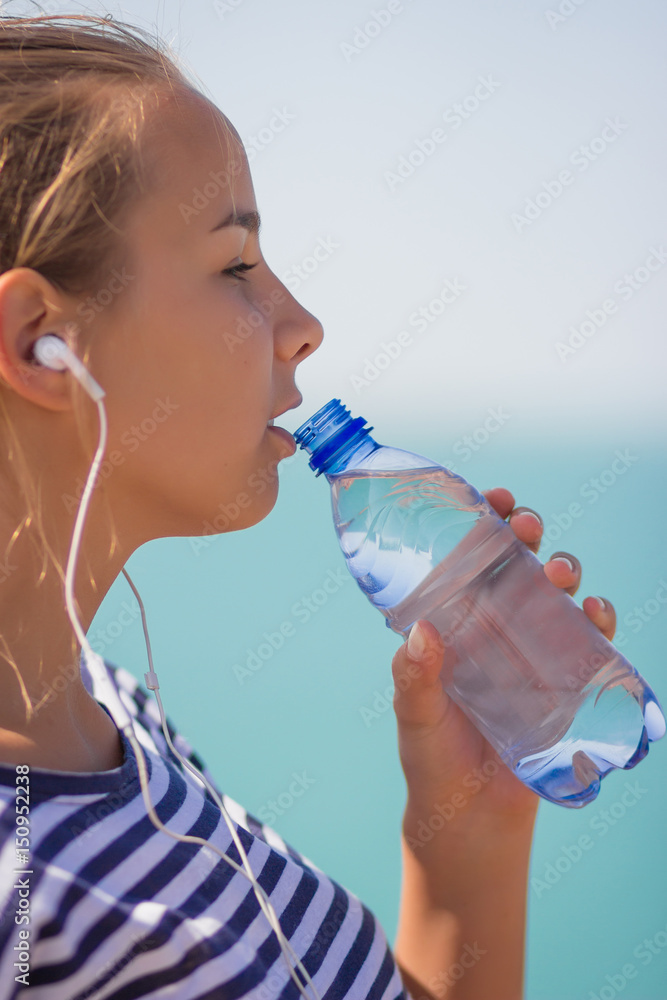 Sports girl drinks water during a workout on the beach. The girl drinks water during fitness outdoors Sports girl drinks water during a workout on the beach. The girl drinks water during fitness outdoors