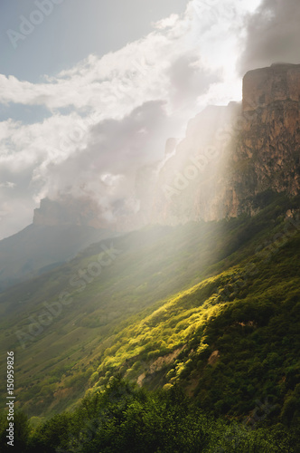 Vertical landscape, the sunlight breaking through the clouds locally illuminates the slope section at the foot of the Caucasian rocks of Upper Balkaria © yanik88