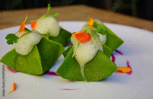 Vegan green raw kimchi dumplings with coconut foam and edible flowers photo