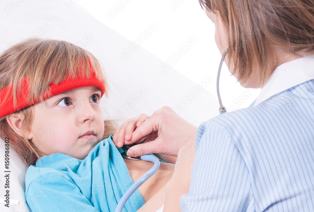 Sick little girl in bed. Mother or female doctor with stethoscope sitting near the bed. Portrait of illnes kid with fever, resting at home. Child taking medicine. Sick little girl in bed. Mother or female doctor with stethoscope sitting near the bed. Portrait of illnes kid with fever, resting at home. Child taking medicine.
