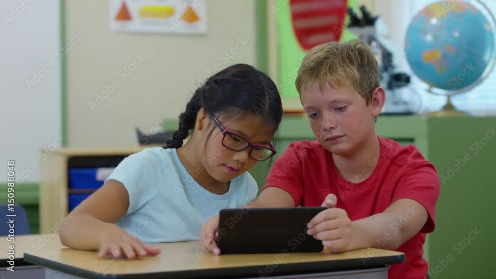 Two students work on digital tablet together in school classroom Two students work on digital tablet together in school classroom