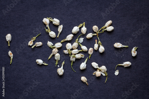 Fototapeta Naklejka Na Ścianę i Meble -  Tea from white dried jasmine buds and flowers on a black surface, top view