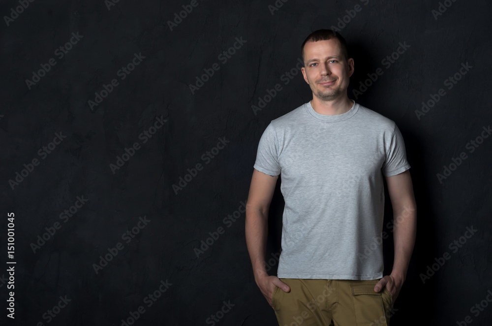 Portrait of laughing young man with hands in pockets leaning against black wall. Portrait of laughing young man with hands in pockets leaning against black wall.