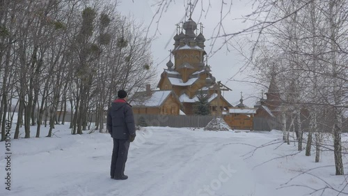 Man Walks by Snowy Alley Xvii Century Church Christian Wooden Monastery Skit Vsekh Svyatykh in Sviatogorskaya Lavra Religious Man Crossing Himself photo