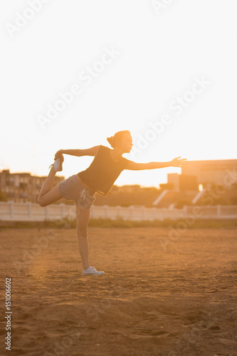 Young girl practices yoga on the beach in the morning at the dawn of the sun