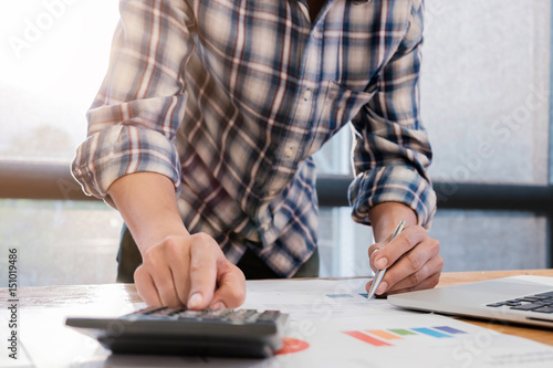 Close up of accountant man or banker making calculations and laptop conmputer on wooden desk in office with morning light. Savings, finances and economy concept photo