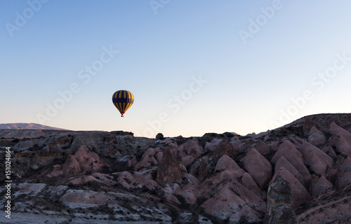 hot air balloon rises very high in blue sky above white clouds, bright sun shines