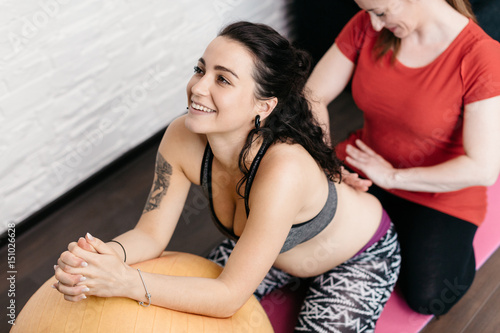 Pregnant woman enjoying a back massage from her midwife. Doula stroking a back of a smiling pregnant woman relaxing on a fitness ball.