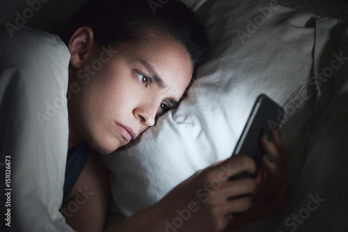 Donna usa smartphone a letto, gelosia o insonnia  photo