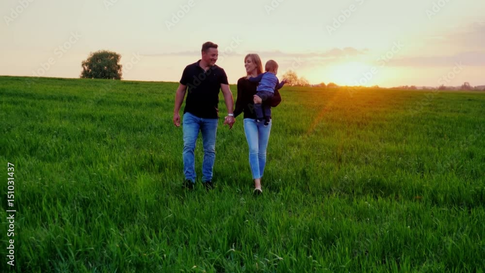 Young happy family with baby. They go to the picturesque green field at sunset. Steadicam shot Young happy family with baby. They go to the picturesque green field at sunset. Steadicam shot