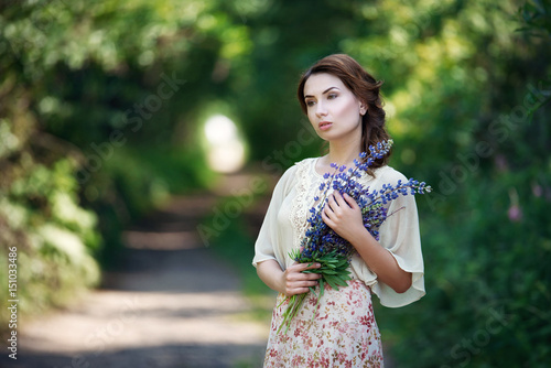 Portrait of pretty young woman walking in a fairy forest with bouquet of flowers.
