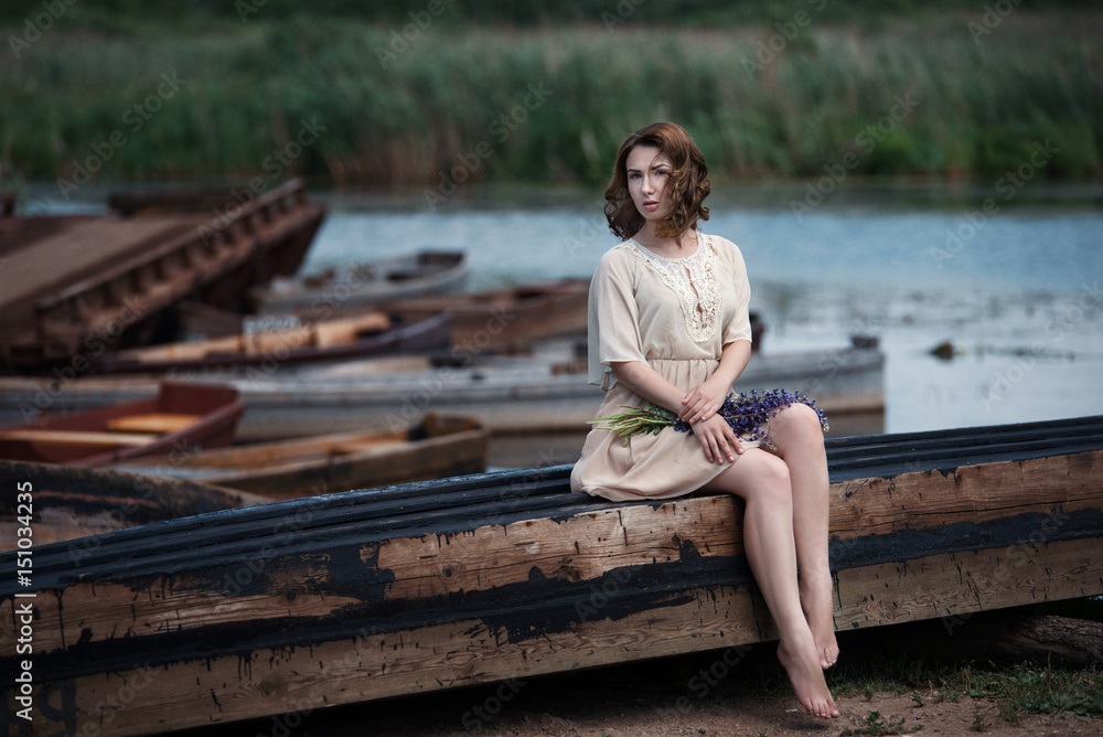 Portrait of pretty young woman sitting in the boat on river bank.