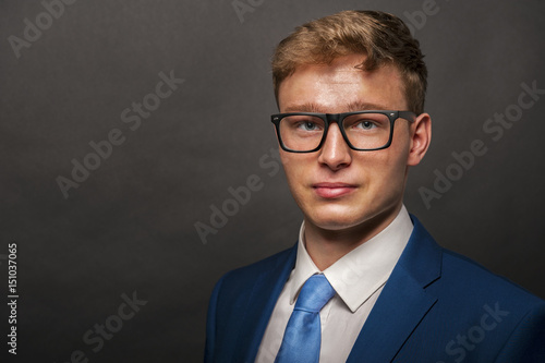 Young handsome man in blue suit with glasess smiling on dark background