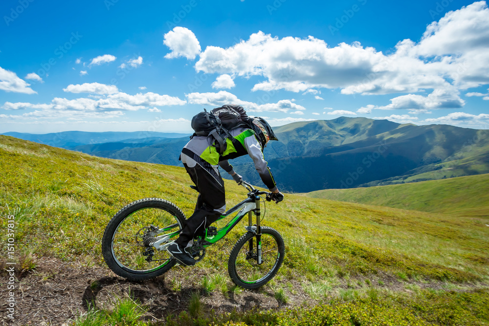 A man is riding bicycle, on the background of mountains and blue sky. Beautiful summer day.