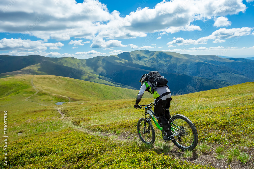 A man is riding bicycle, on the background of mountains and blue sky. Beautiful summer day.