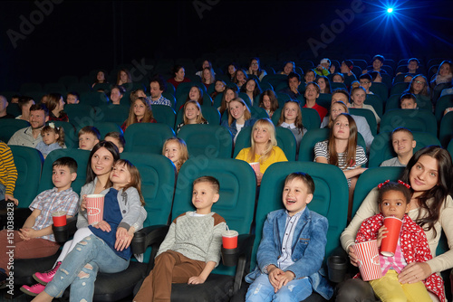 Cute little kids smiling and laughing while watching a cartoon at the local movie theatre people entertaining excitement expressive funny laughter enjoyment elementary lifestyle leisure concept.