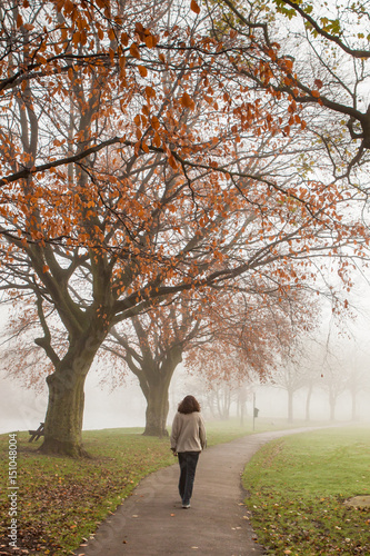 A woman walks through a misty park in the Autumn, with red leaves on the trees