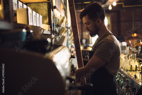 Young male barista preparing drink at coffee machine