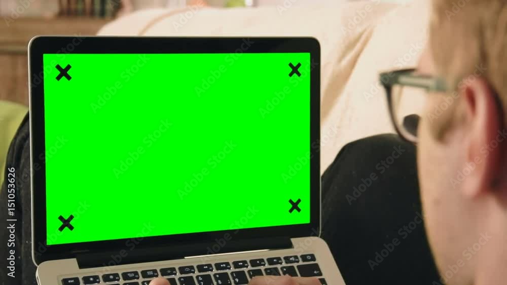 Young man laying on the sofa looking at laptop computer with green screen Young man laying on the sofa looking at laptop computer with green screen