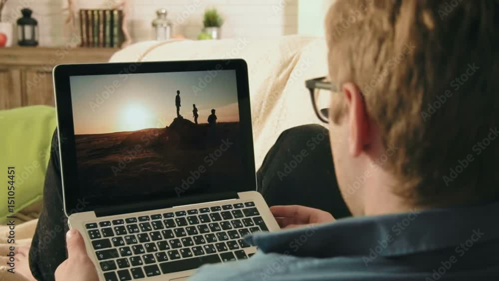 Young man looking at pictures in social network using laptop computer looking for inspiration Young man looking at pictures in social network using laptop computer looking for inspiration