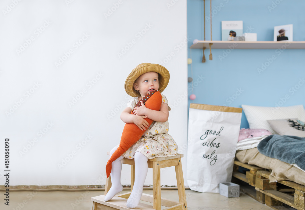 Little girl sitting on a chair and holding a toy fish in room at home.