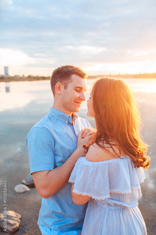 Young beautiful couple in love staying and kissing on the beach on sunset. Soft sunny colors. Young beautiful couple in love staying and kissing on the beach on sunset. Soft sunny colors.