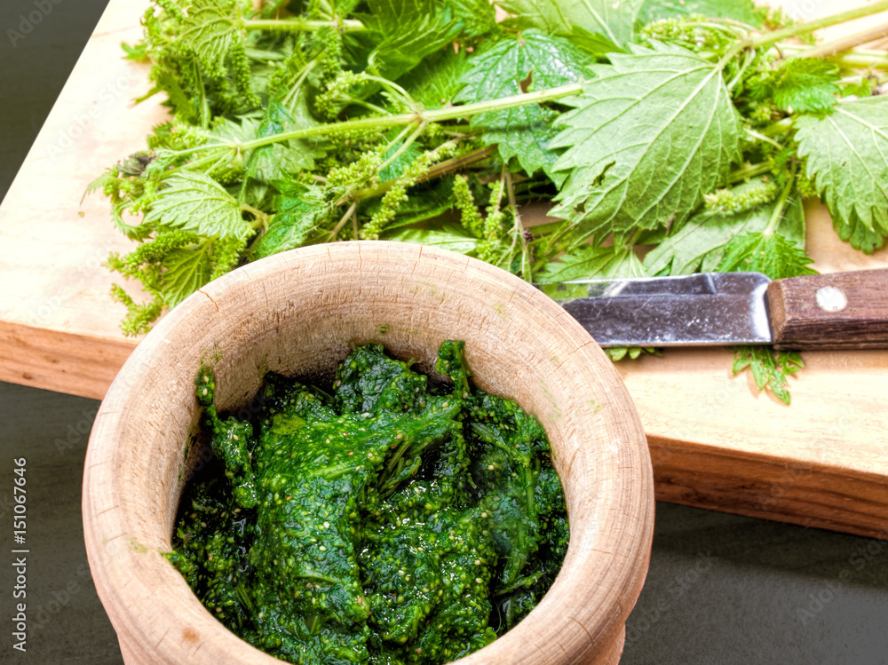 cooked and raw nettles on a wooden board and in a rustic mortar