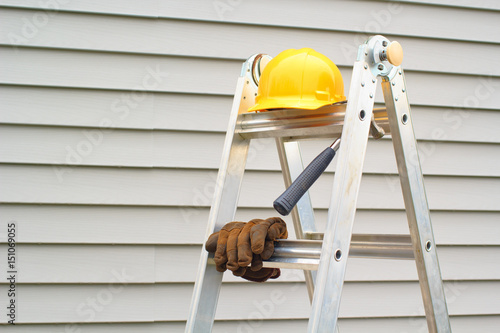 Stepladder, hardhat, gloves and hammer with house siding background
