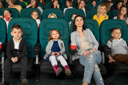 Full length shot of a beautiful young woman smiling watching a movie with her kids at the local cinema entertainment family parenting motherhood kids mother parent leisure activity happiness concept.