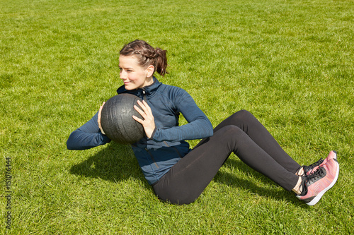 Frau bei Fitnesstraining mit Gewichtsball im Garten