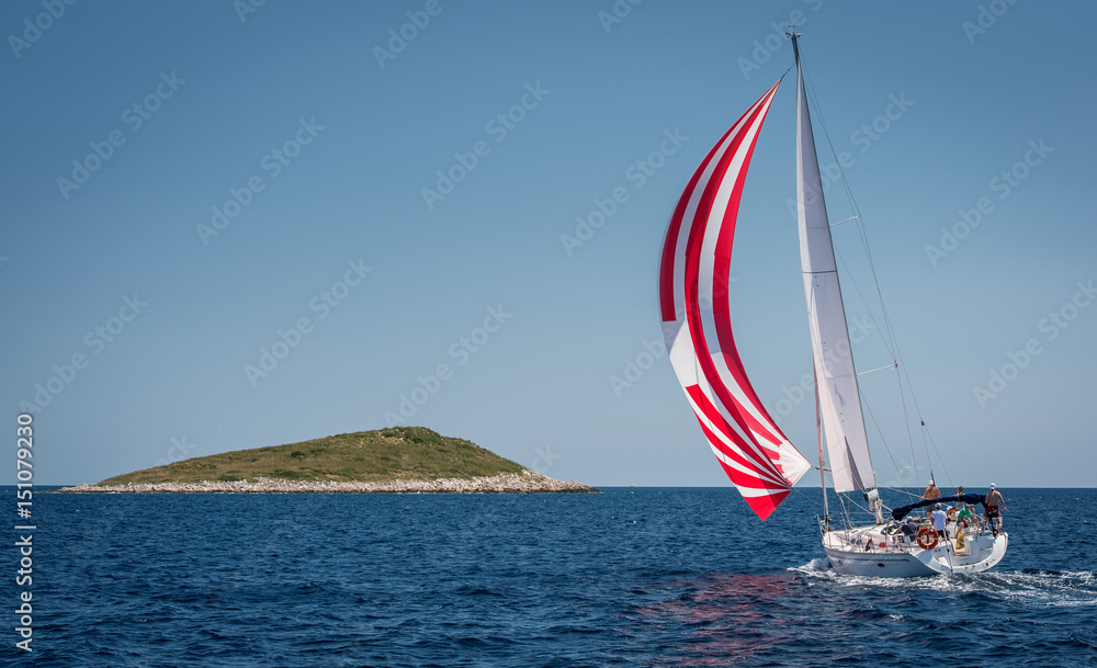 Naklejka premium Sailing boat with spinnaker approaching small island in Croatia