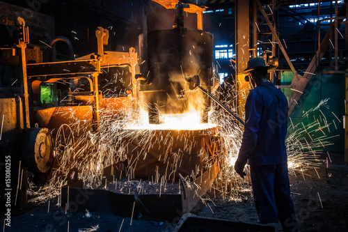 Foundry worker pouring hot metal into cast. Molten metal. Left over material from the steel manufacturing process is poured away on at a Steel Foundry photo