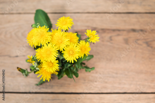 Bouquet of yellow dandelions with leaves on an old wooden table, top view