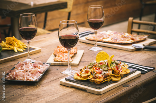 Traditional atmosphere with colorful plate of nachos flavored with vegetables and glass of red wine on rustic wooden table