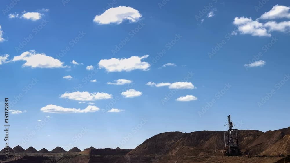 Wide shot of operating mine with dragline excavators loading ore in the background under blue sky with moving clouds. Bauxite quarry. Wide shot of operating mine with dragline excavators loading ore in the background under blue sky with moving clouds. Bauxite quarry.