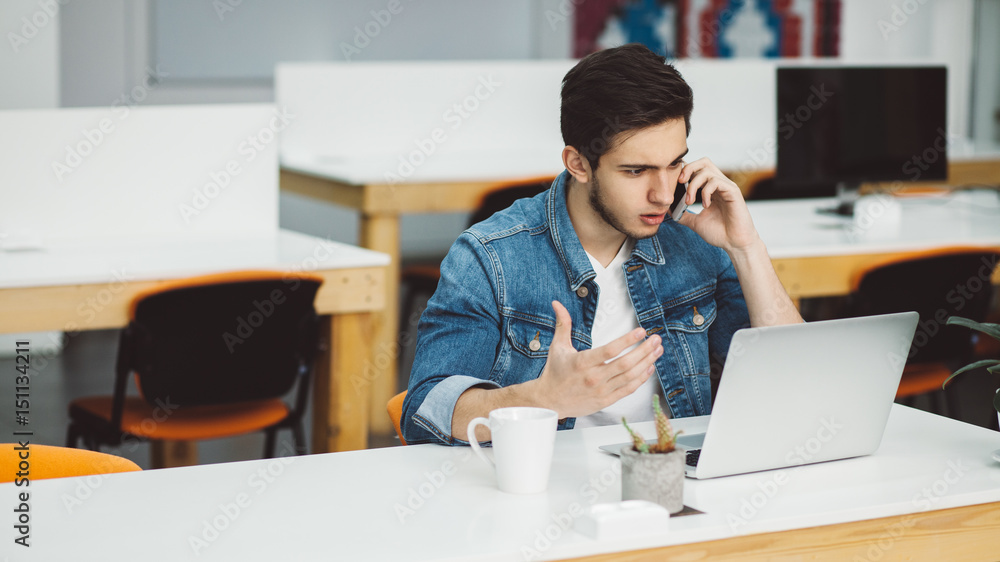 Young busy man with beard working on laptop and using mobile phone Young busy man with beard working on laptop and using mobile phone