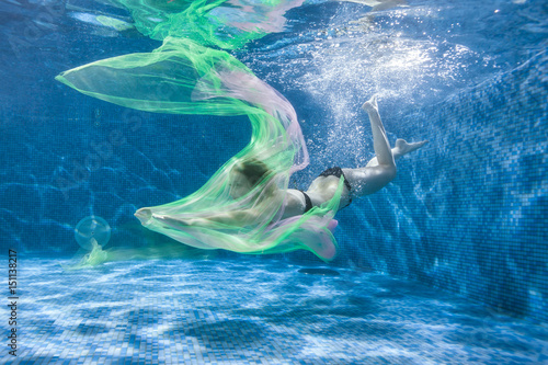 At the bottom of the pool  a woman with a colored fabric dives.