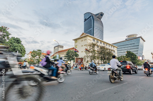 People driving motorbikes on the street in Phnom Penh, Cambodia. Modern skyscrapers on the background photo
