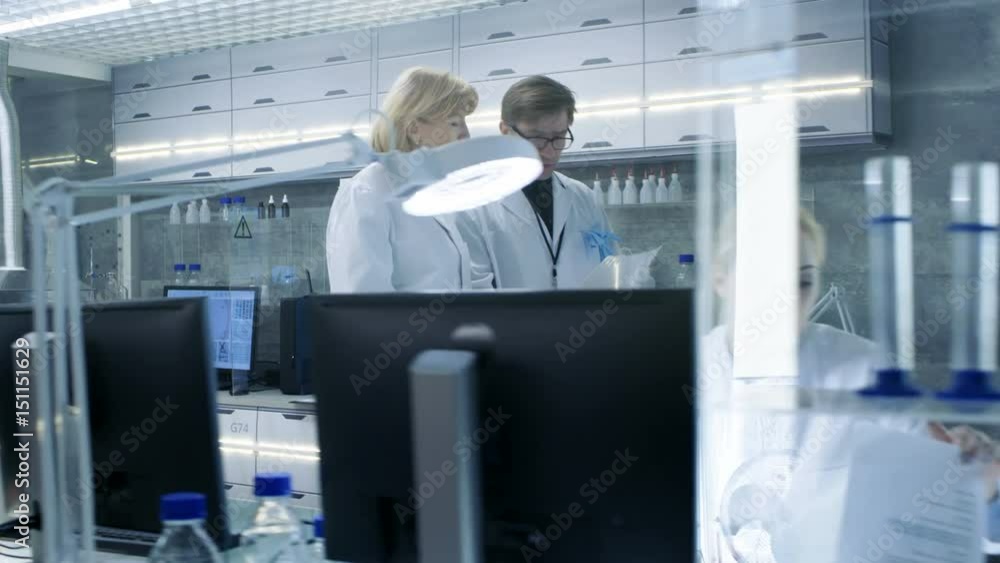 Female and Male Senior Scientists Walking Through Busy Modern Laboratory. They Have Discussion about Documents. Shot on RED EPIC-W 8K Helium Cinema Camera. Female and Male Senior Scientists Walking Through Busy Modern Laboratory. They Have Discussion about Documents. Shot on RED EPIC-W 8K Helium Cinema Camera.