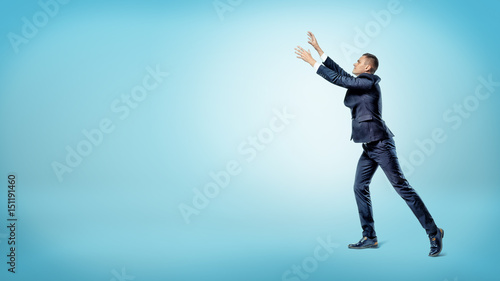 A businessman in side view with both hands raised up trying to catch something above.