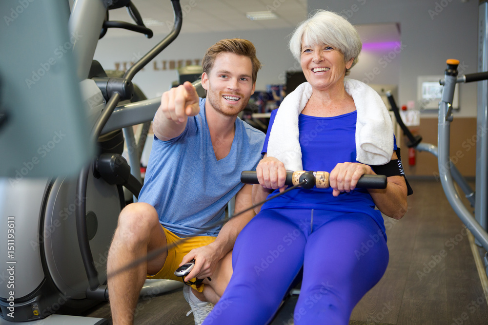 Fototapeta premium personal trainer with senior woman using rowing machine