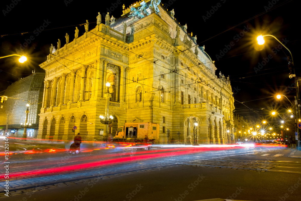 The Prague intersection at night has a long running light, and the light from the light towers.