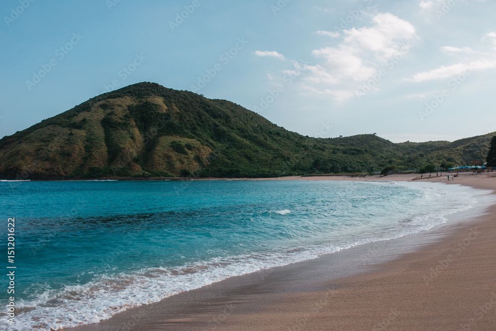 Landscape with a tropical beach with green hills, rocks on the background, water is azure and sand is white, Indonesia, Lombok
