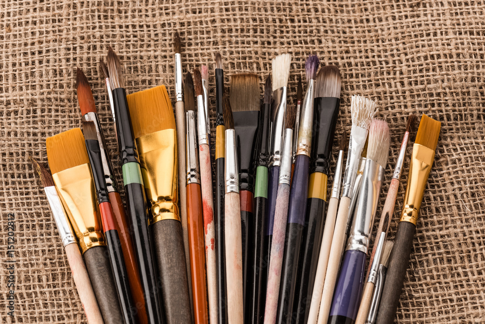 Close-up top view of various paintbrushes collection on sackcloth Close-up top view of various paintbrushes collection on sackcloth