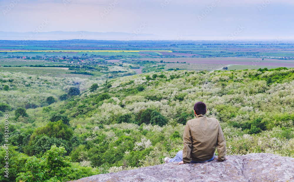 Man sitting on a rock above the valley watching distant foggy mountains