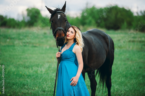 Girl in meadow with a horse on green grass